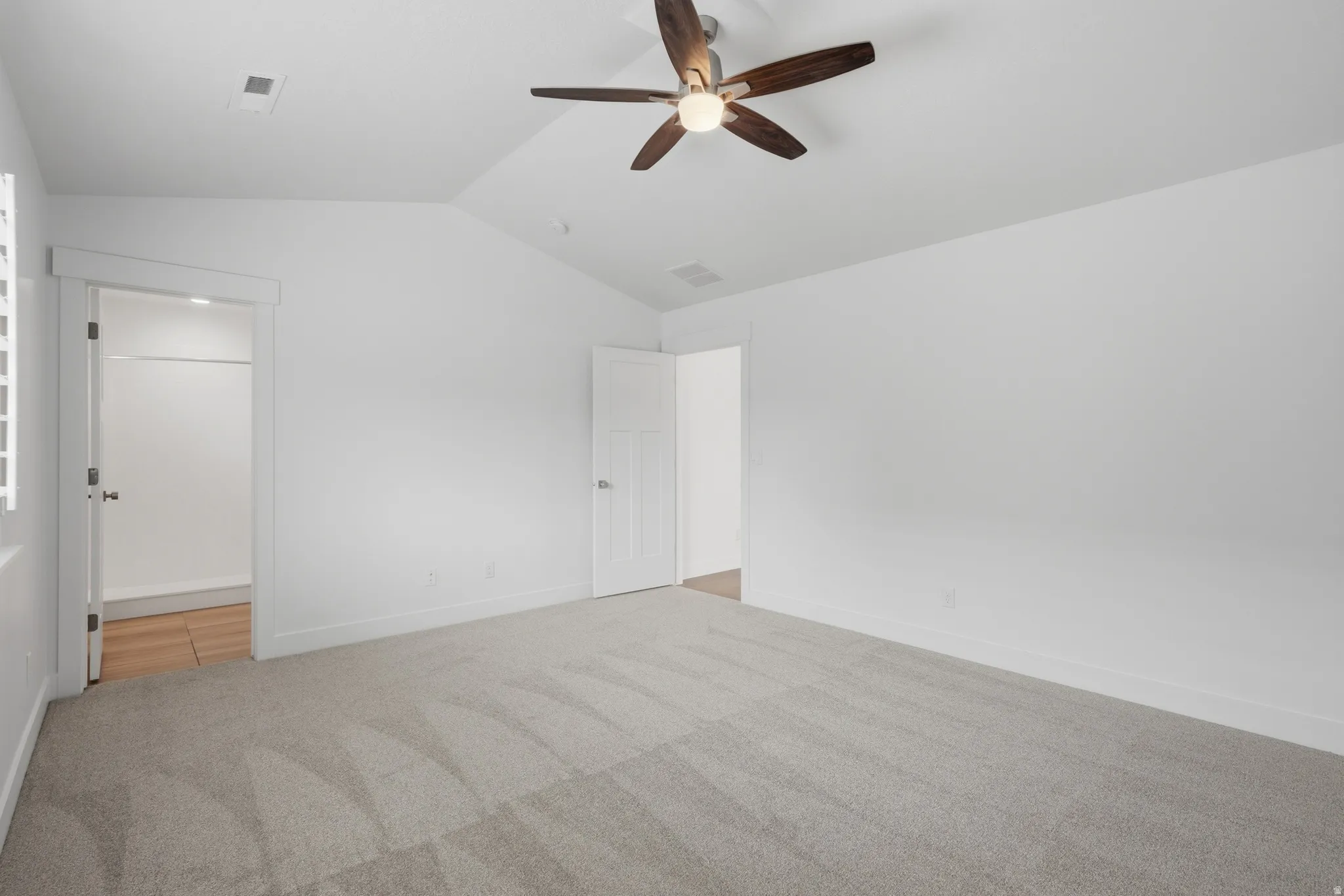 Bright room featuring a vaulted ceiling and a wood-finish ceiling fan