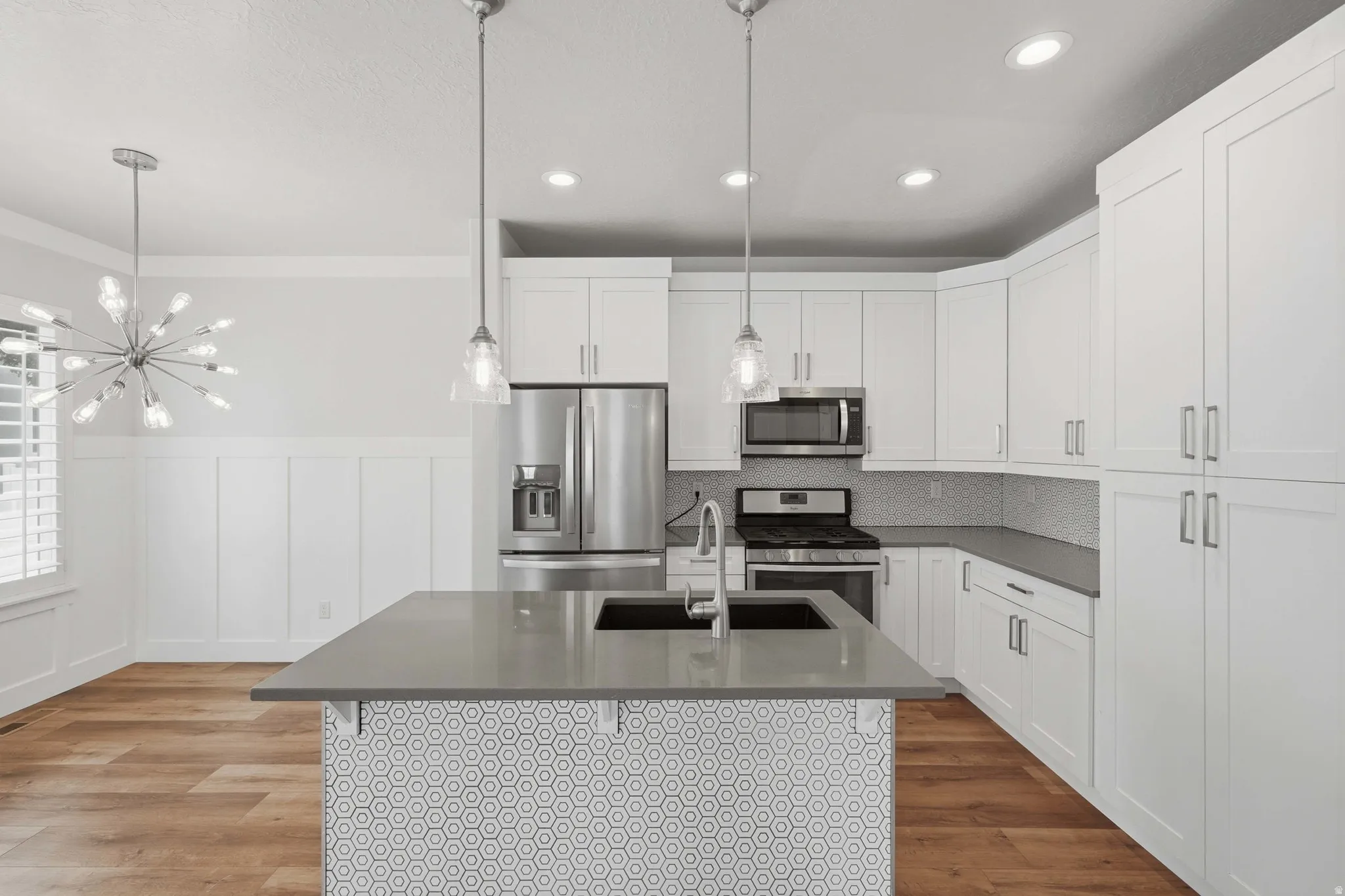 Kitchen featuring a center island with pendant lighting, white cabinetry, stainless steel appliances, and wood-finish flooring