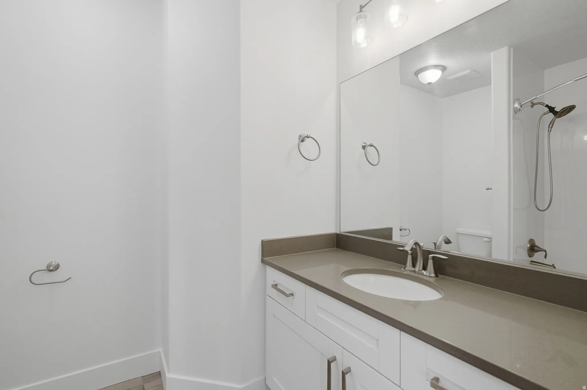 White vanity with flat panel cabinetry, brushed nickel hardware, and a gray countertop featuring an undermount sink
