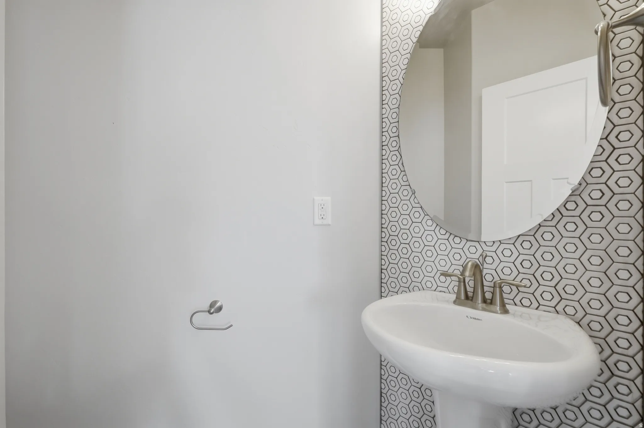 Pedestal sink with a brushed nickel faucet, set against a geometric hexagonal tile accent wall