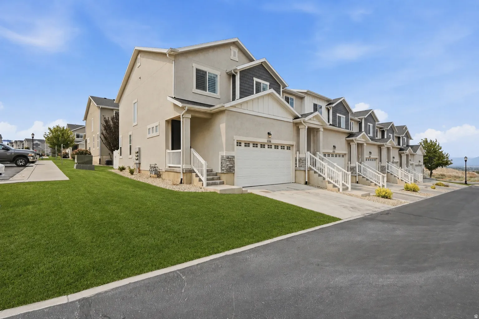 Contemporary townhome exterior featuring light-colored stucco, dark siding accents, a two-car garage, white railings, and a manicured lawn