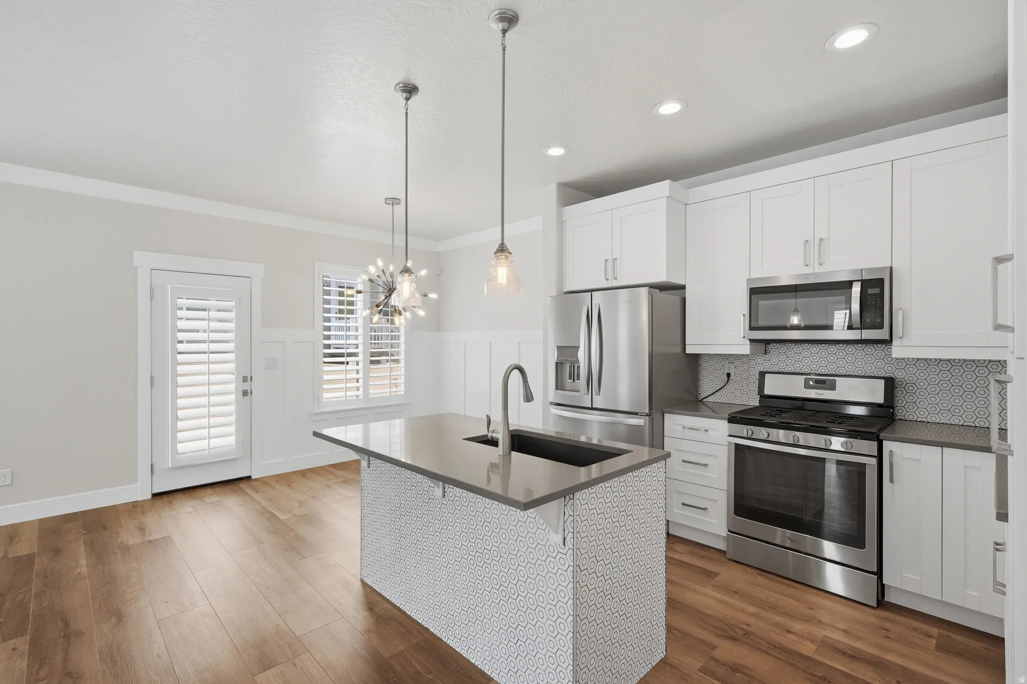 Modern kitchen featuring white shaker cabinetry, stainless steel appliances, a center island with sink, and wood-finish flooring