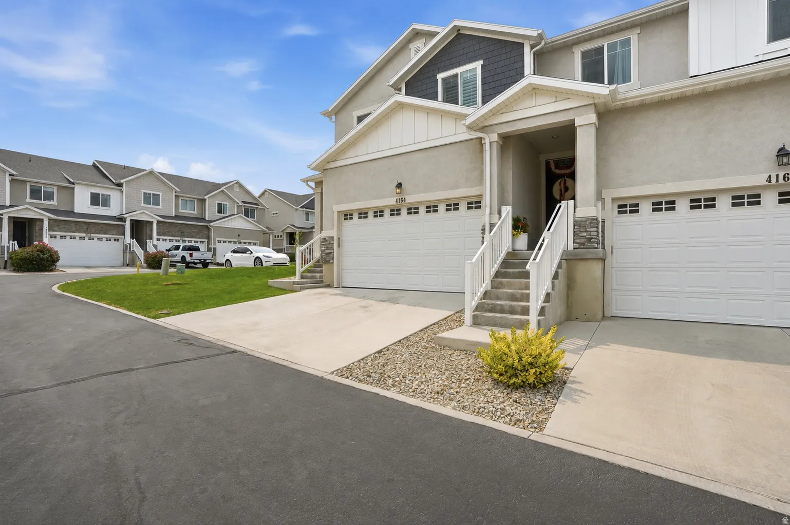 Contemporary townhome exterior featuring an attached two-car garage, covered entry porch, white railings, and stone accents