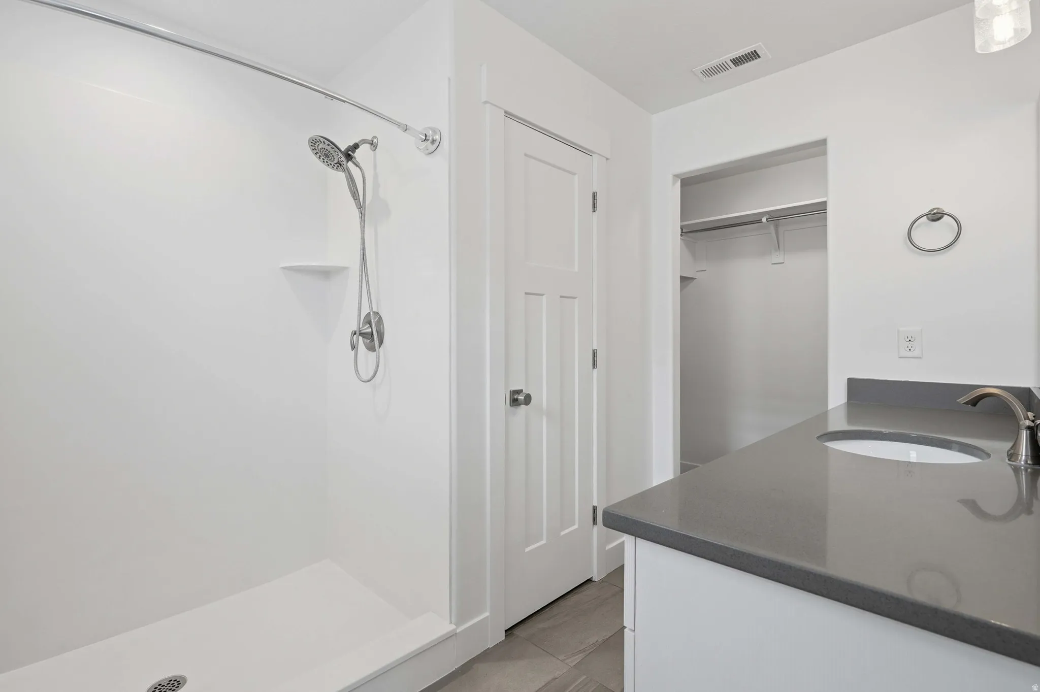 Shower with a handheld spray fixture, a single-sink vanity with a dark countertop, and a walk-in closet with shelving and hanging rods