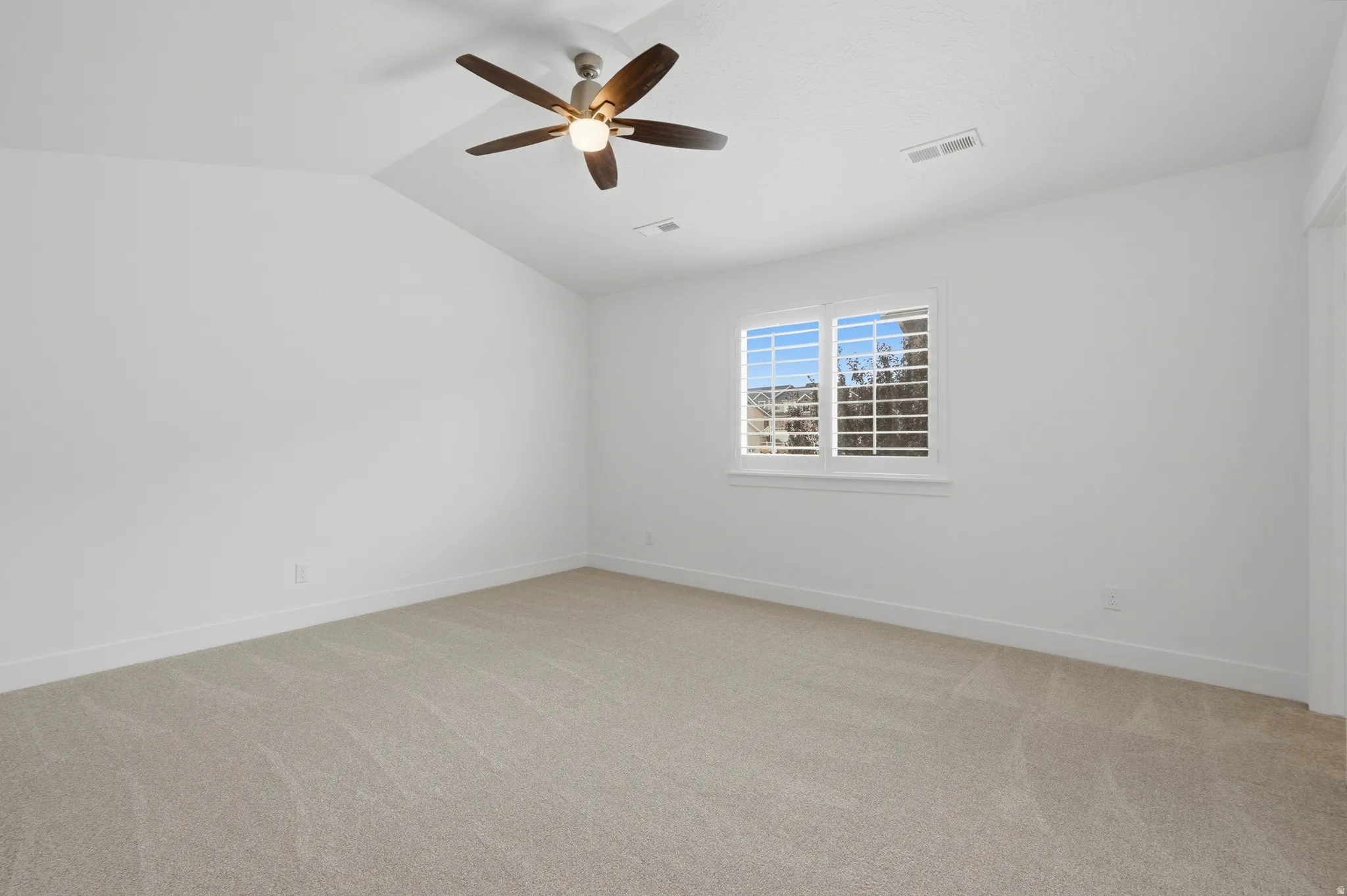 Carpeted room featuring a vaulted ceiling with a ceiling fan, white window shutters, and white baseboards