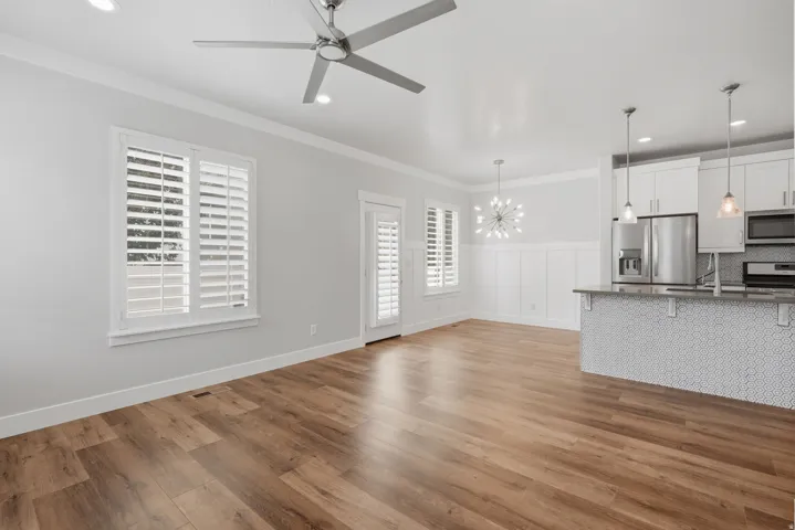 Open-concept living area featuring wood-finish flooring, white plantation shutters, and a modern ceiling fan