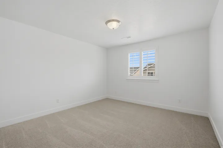 Neutral color palette with textured carpeting, white walls, and a window featuring plantation shutters
