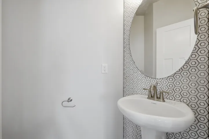 Pedestal sink with a brushed nickel faucet, set against a geometric hexagonal tile accent wall