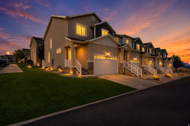 Row of townhomes featuring attached garages, illuminated entryways, and manicured lawns