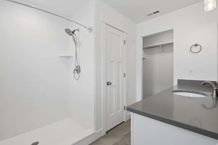 Shower with a handheld spray fixture, a single-sink vanity with a dark countertop, and a walk-in closet with shelving and hanging rods