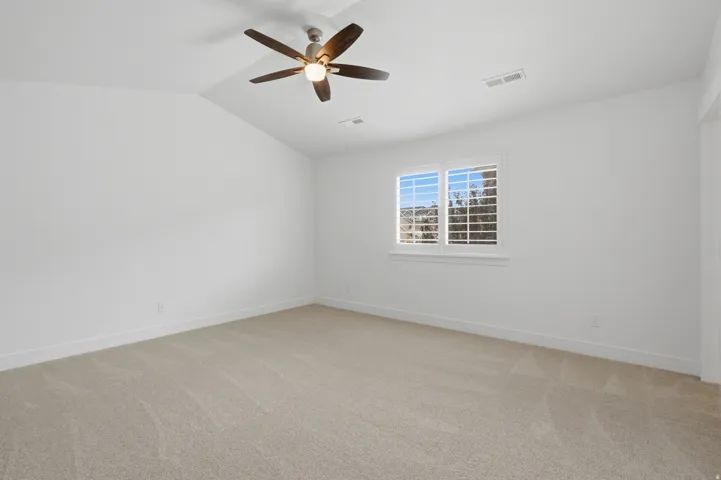 Carpeted room featuring a vaulted ceiling with a ceiling fan, white window shutters, and white baseboards