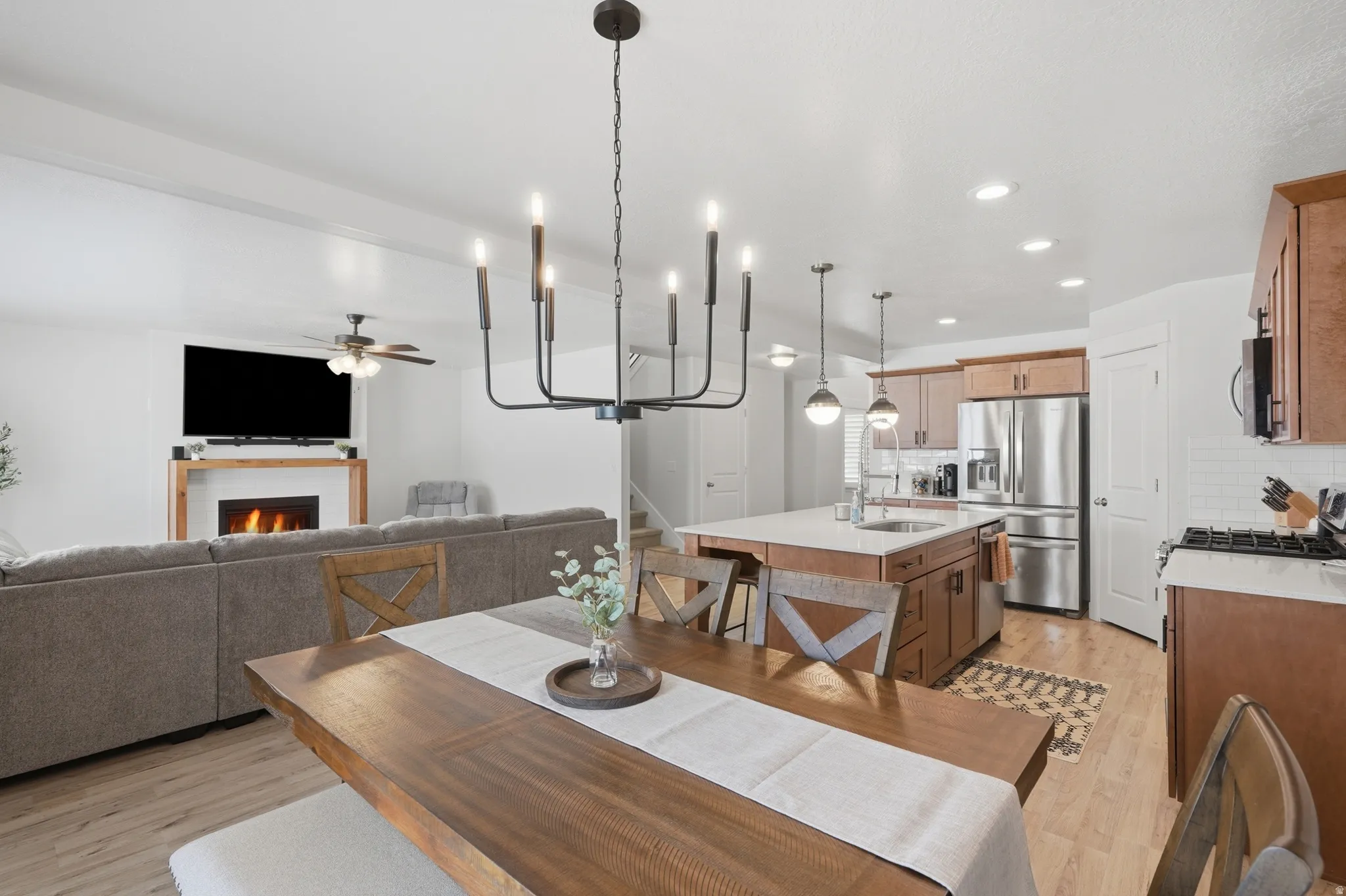 Open-concept living area featuring wood-finish flooring, a contemporary fireplace with a timber mantel, recessed lighting, and a modern chandelier