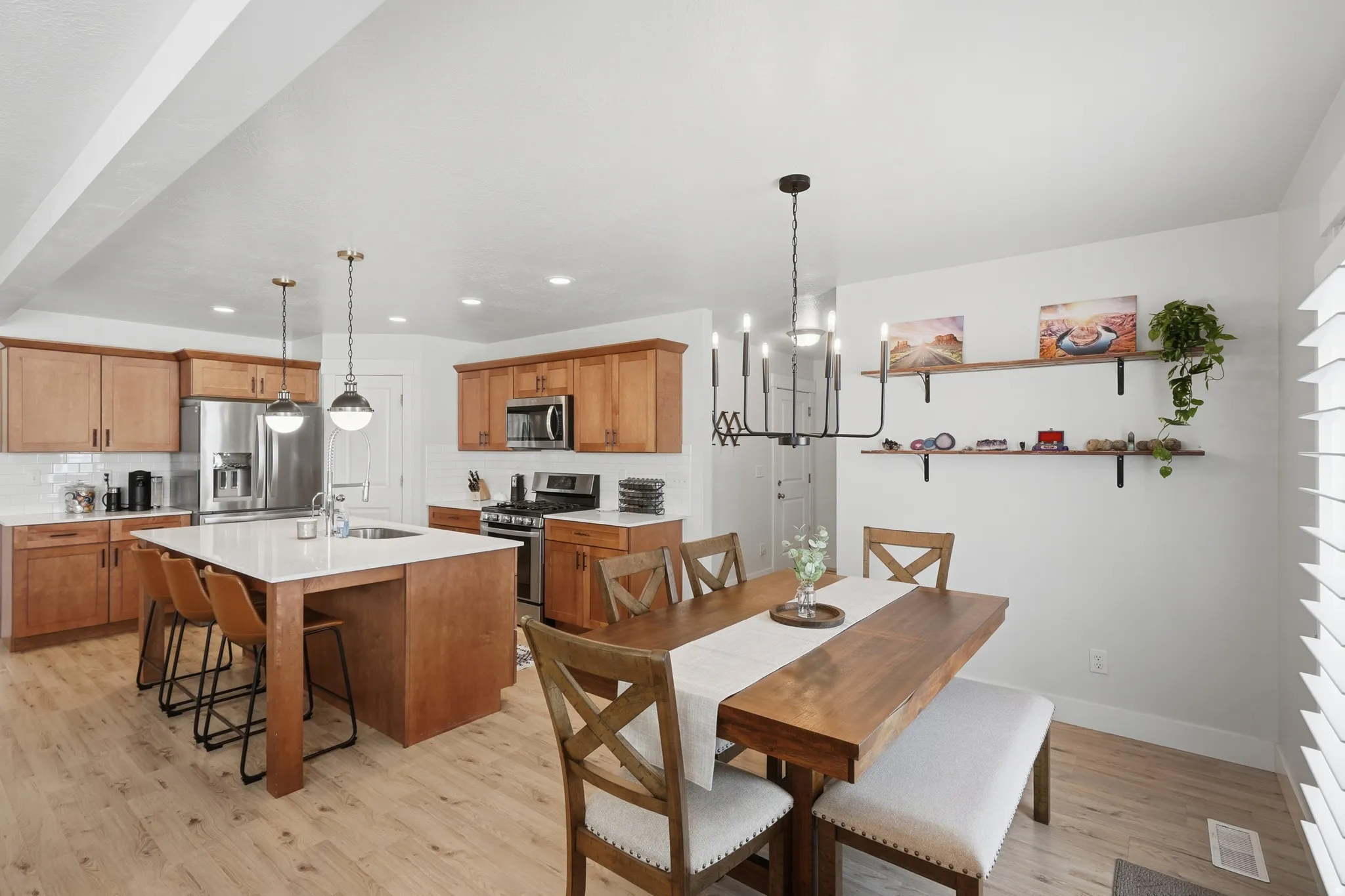 Open-concept kitchen and dining area featuring light wood-finish flooring, a kitchen island with seating, stainless steel appliances, light wood cabinetry, and a subway tile backsplash
