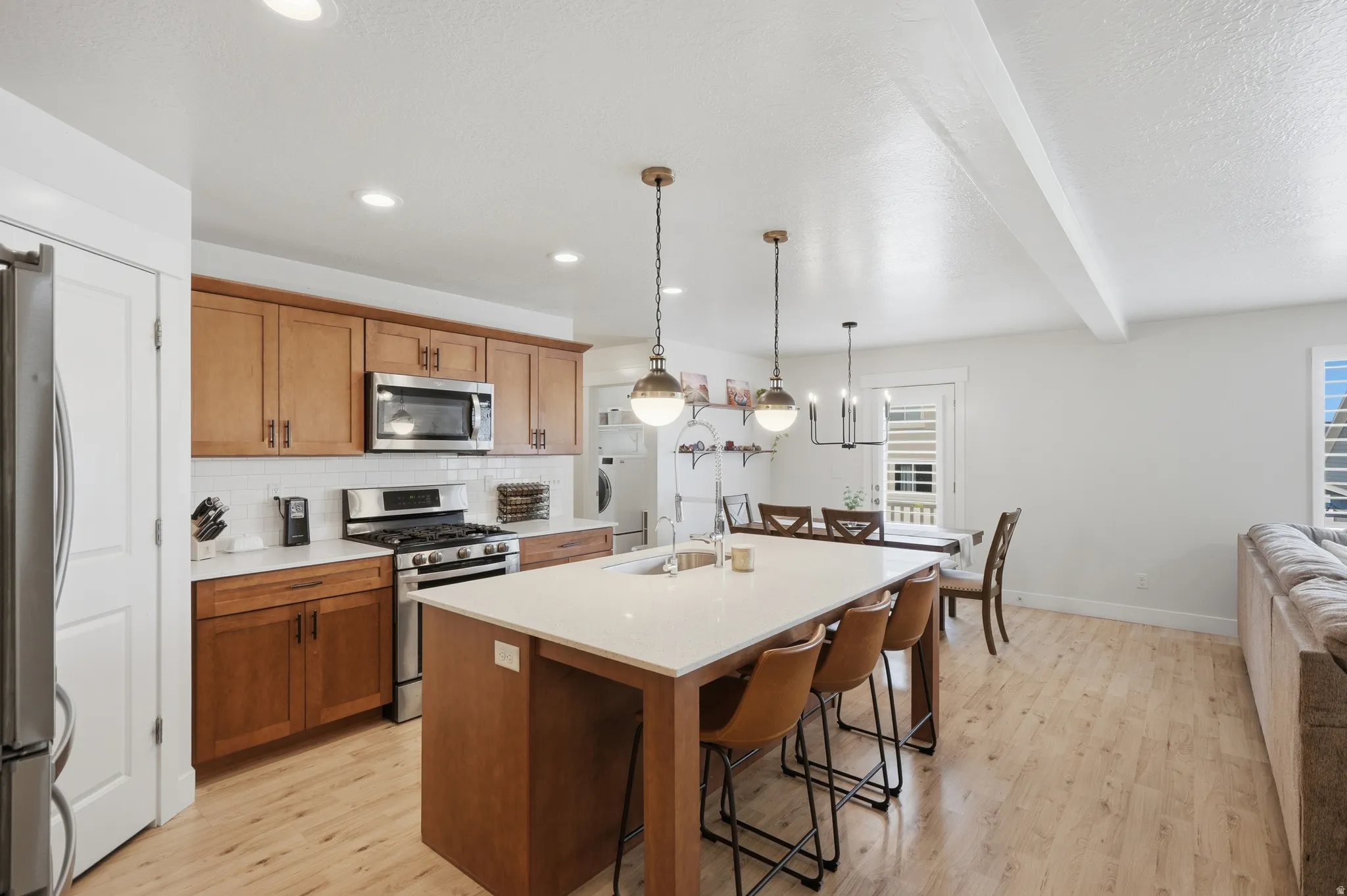 Open-concept kitchen featuring an island with built-in sink, stainless steel appliances, wood-finish cabinetry, and light wood-finish flooring