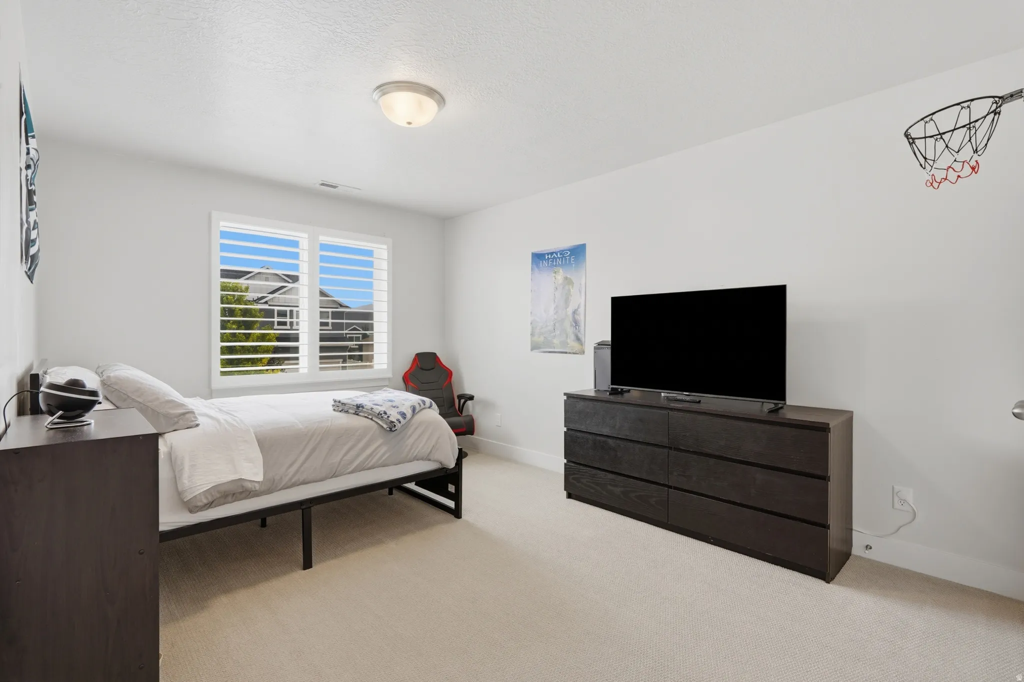 Spacious room featuring light-colored carpeting, large window with plantation shutters, a contemporary ceiling light fixture, and white painted walls