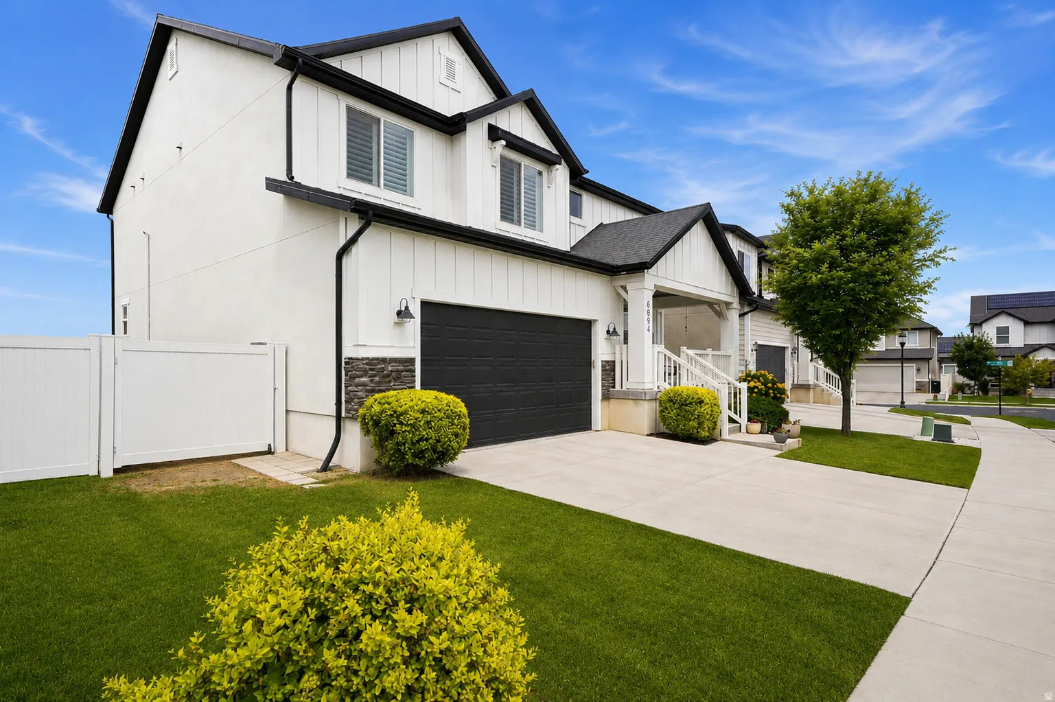 Modern two-story townhome featuring white board and batten siding, dark trim, and an attached garage with a black door