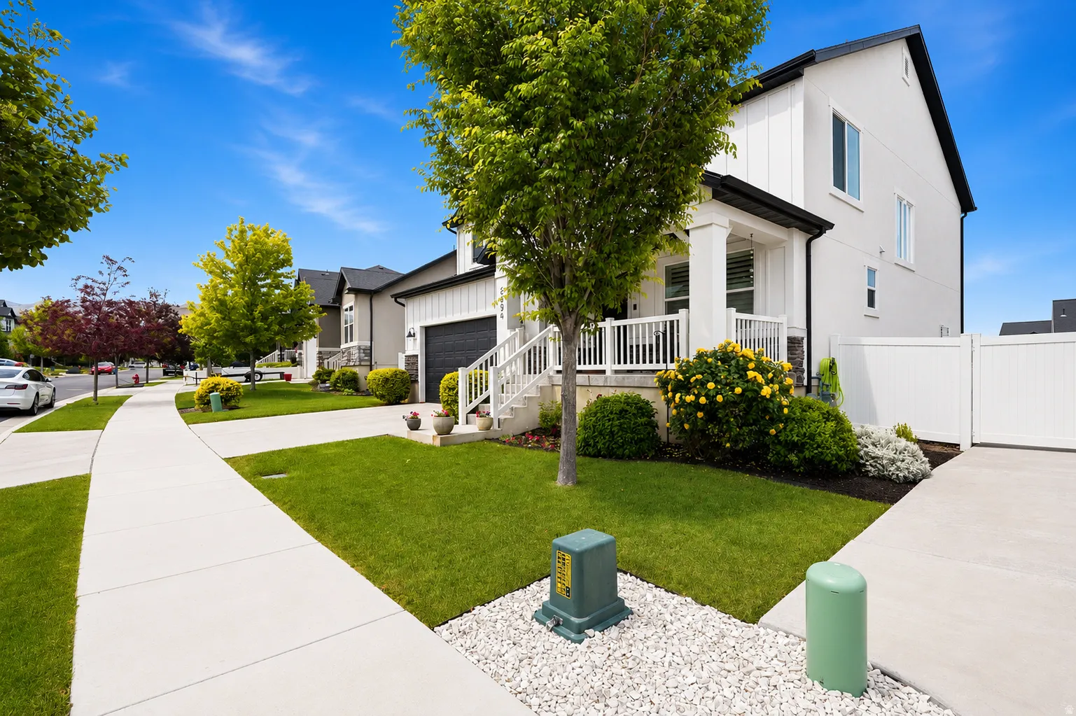 Contemporary exterior featuring white vertical siding, black trim, a covered porch with white railings and columns, a dark garage door, and a concrete driveway