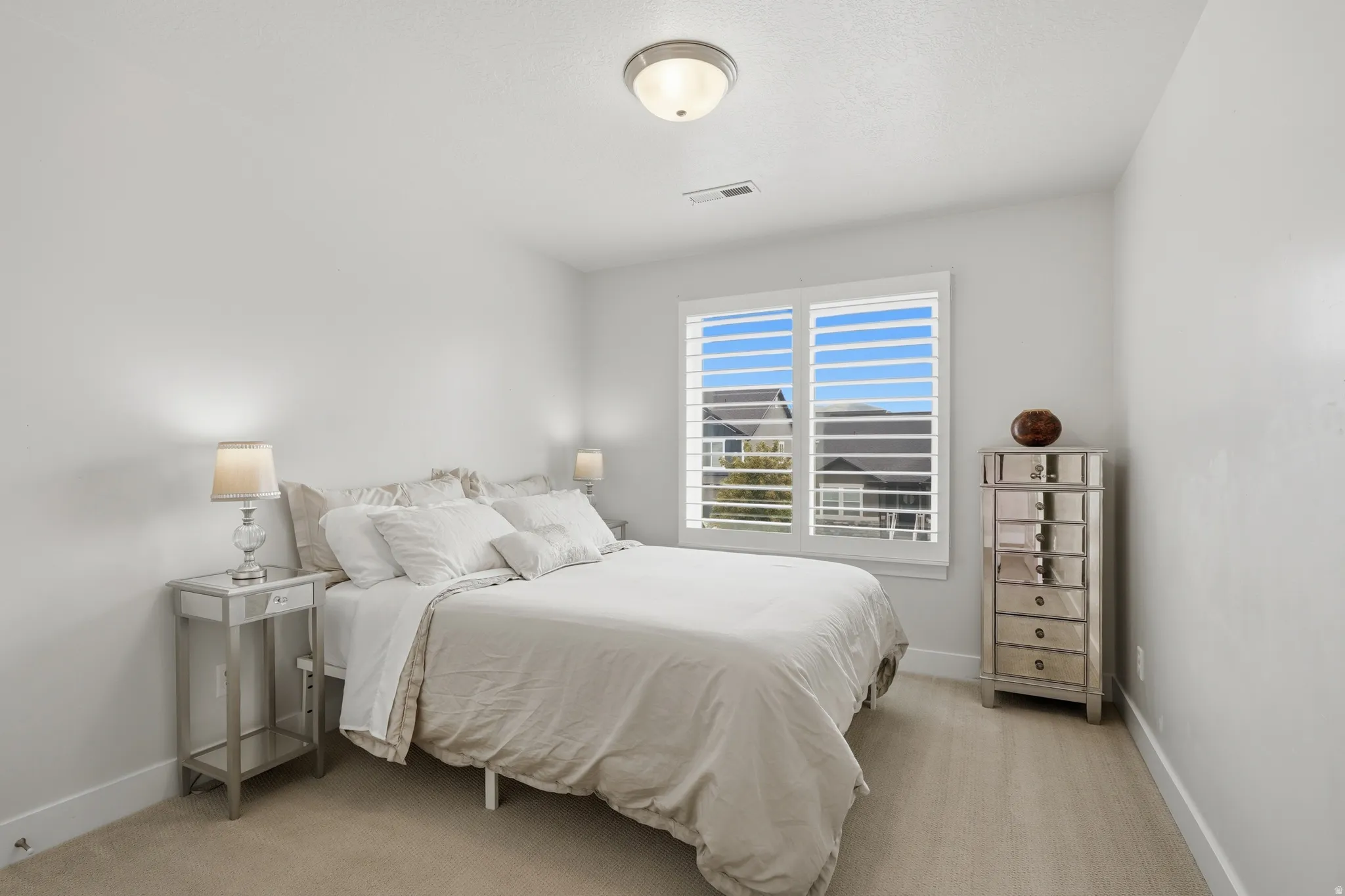 Bedroom featuring light-toned walls, a window with plantation shutters, wood-finish flooring, and an overhead flush-mount light fixture