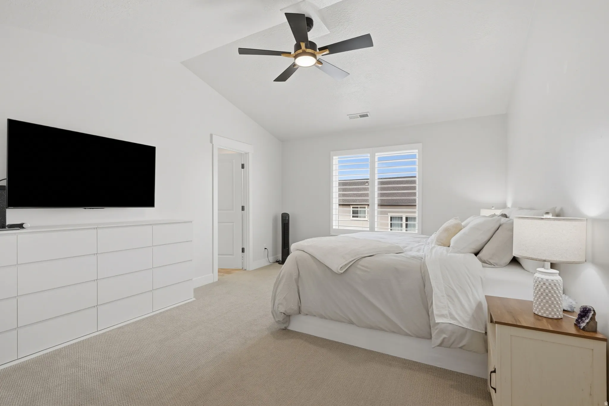 Vaulted ceiling with a contemporary ceiling fan, light-colored carpeting, white walls, and a window featuring horizontal blinds