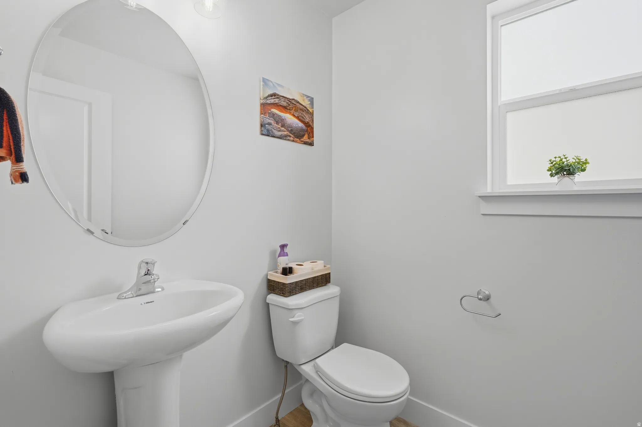 Bathroom featuring a pedestal sink with chrome faucet, an oval frameless mirror, and a window with white trim