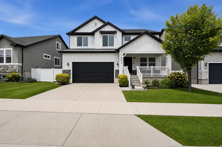 Modern farmhouse exterior featuring black trim, white vertical siding, a covered porch with white railings, a two-car garage, and a concrete driveway