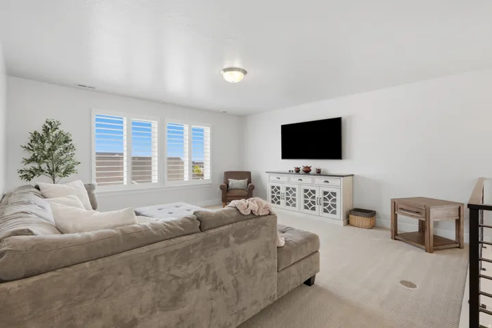 Spacious room featuring multiple windows with louvered shutters, light-toned carpeting, a wall-mounted television, and a built-in console cabinet with decorative glass panels