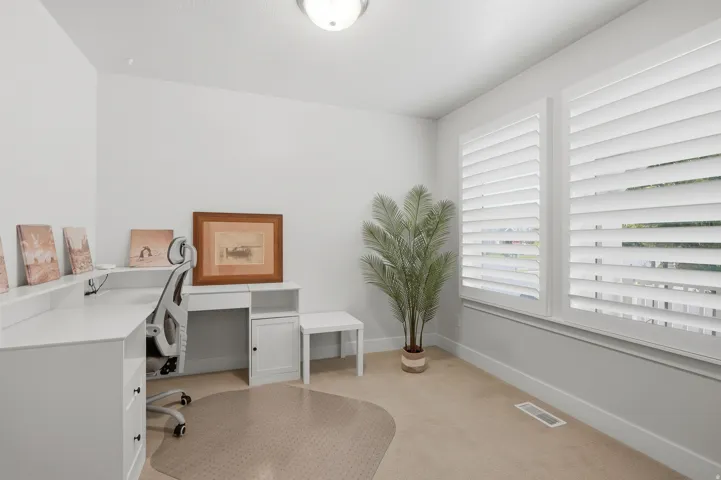 Bright room featuring twin windows with plantation shutters, neutral carpeting, white baseboards, and a flush-mount ceiling light