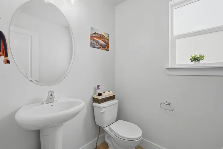 Bathroom featuring a pedestal sink with chrome faucet, an oval frameless mirror, and a window with white trim