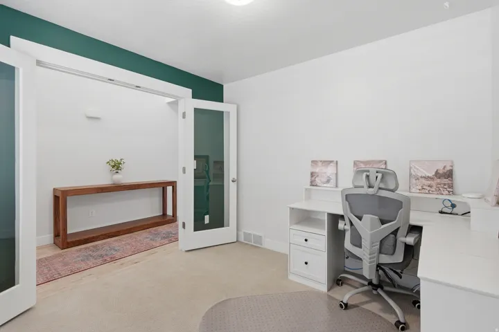 Room with white walls and a deep green accent wall, featuring a carpeted floor, white trim, and a doorway with French doors