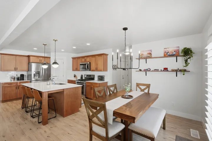 Open-concept kitchen and dining area featuring light wood-finish flooring, a kitchen island with seating, stainless steel appliances, light wood cabinetry, and a subway tile backsplash
