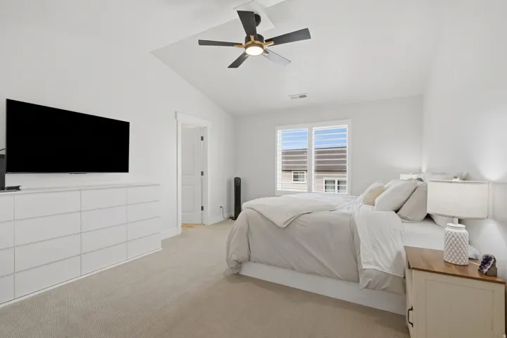 Vaulted ceiling with a contemporary ceiling fan, light-colored carpeting, white walls, and a window featuring horizontal blinds