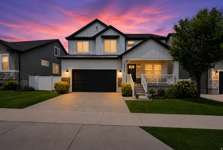 Contemporary exterior with vertical white siding, black trim accents, a covered front porch, and an attached two-car garage