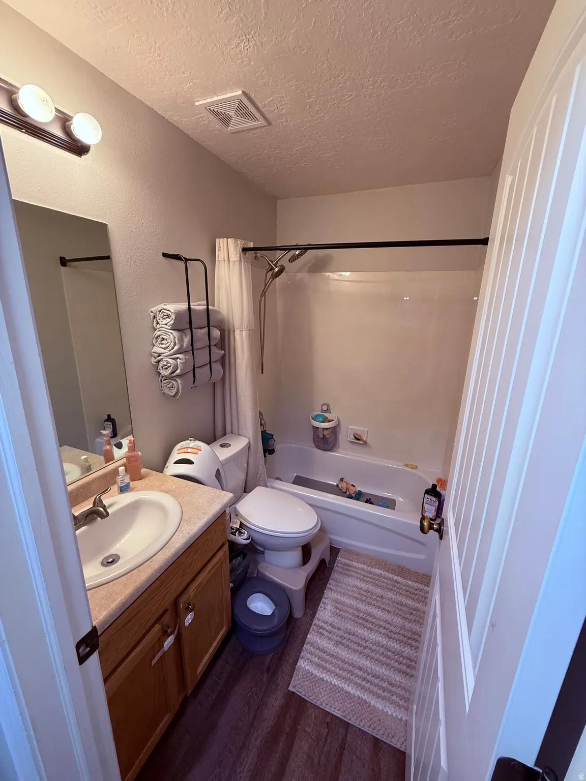 Bathroom featuring a single vanity with wood-finish cabinetry, a built-in tub with shower, and wood-finish flooring