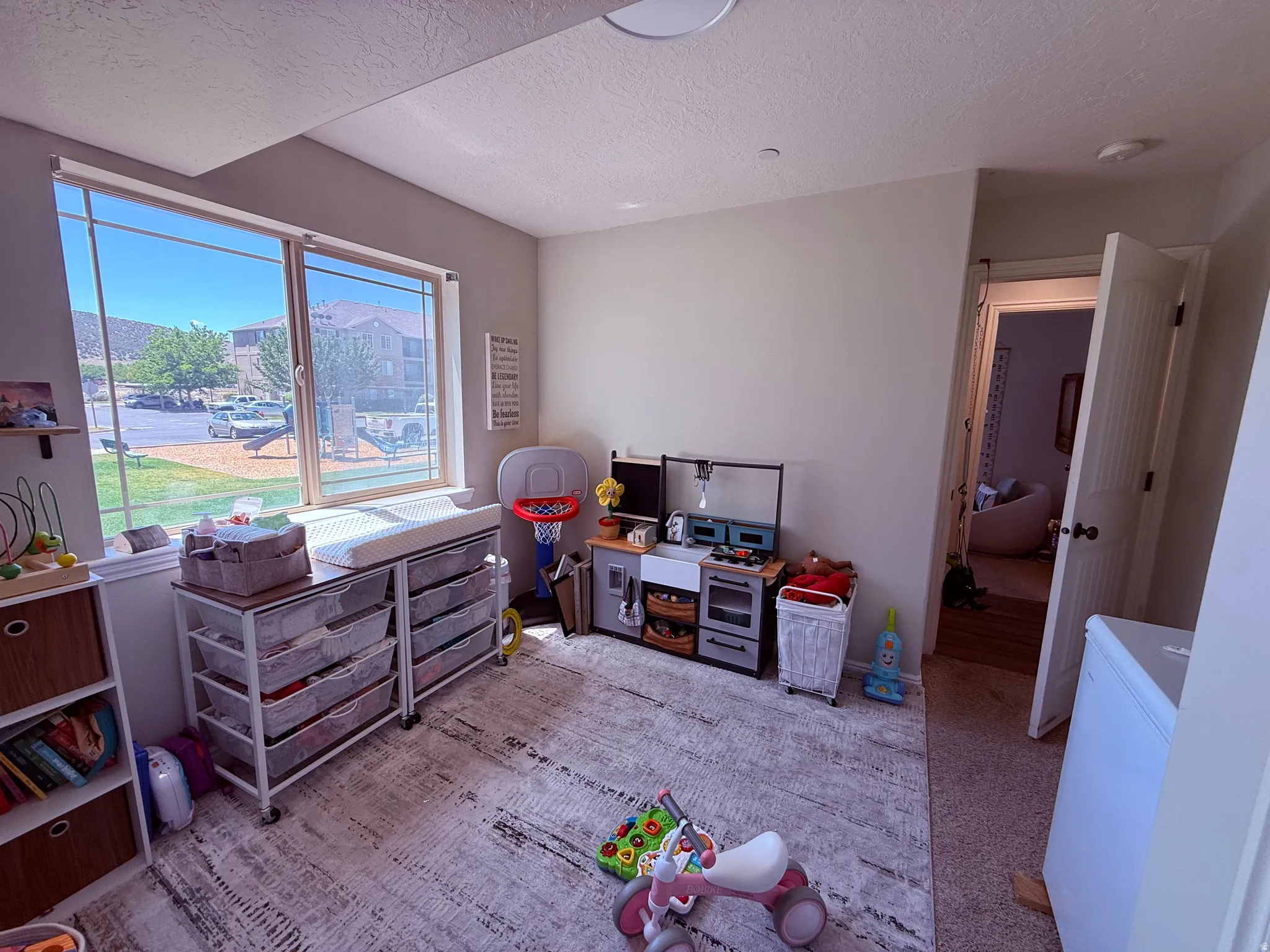 Spacious room featuring a large window with white blinds, light gray walls, and light-colored carpeting