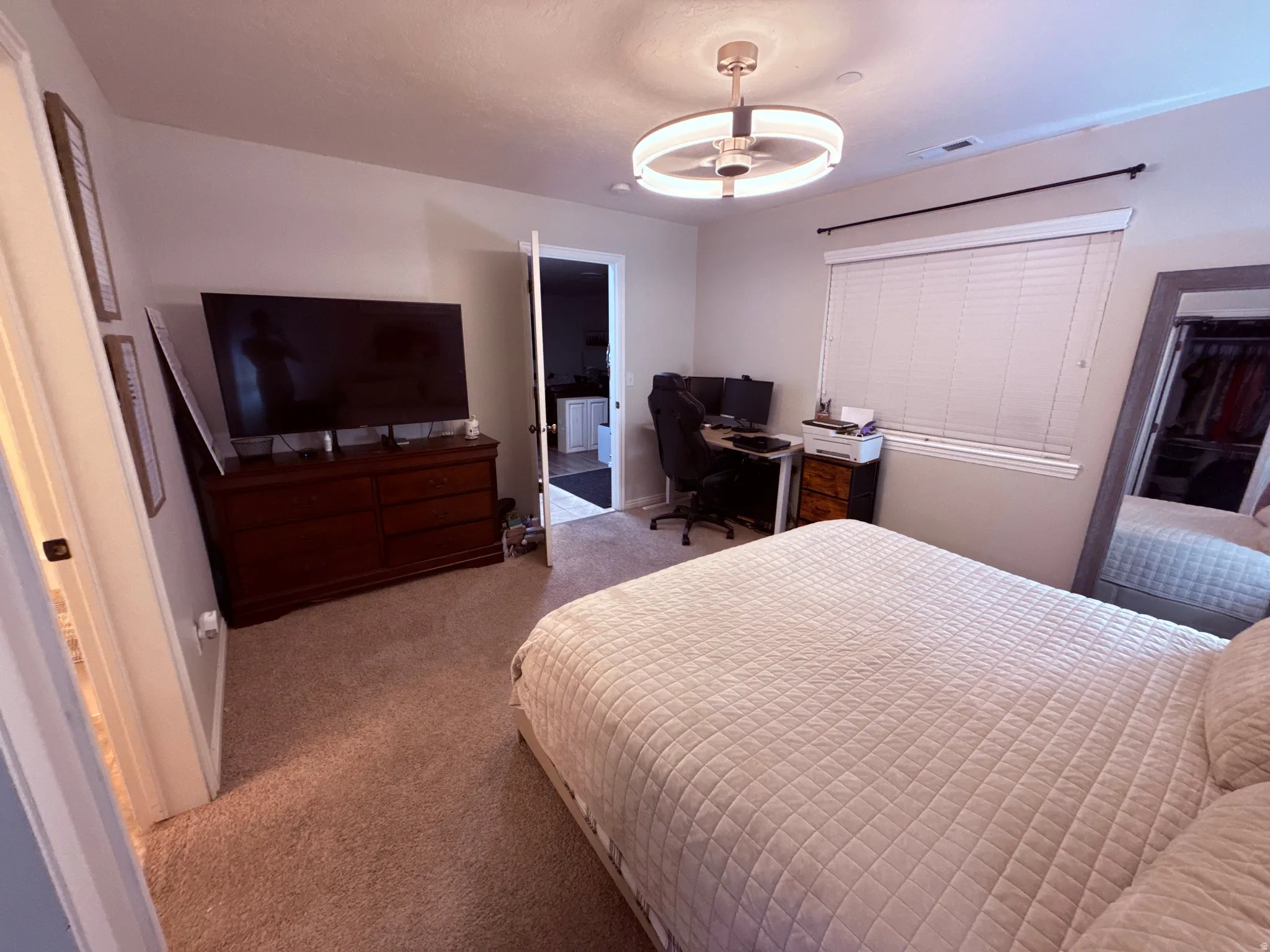 Carpeted bedroom featuring a ceiling fan with integrated lighting, a window with horizontal blinds, and a built-in closet with mirrored doors