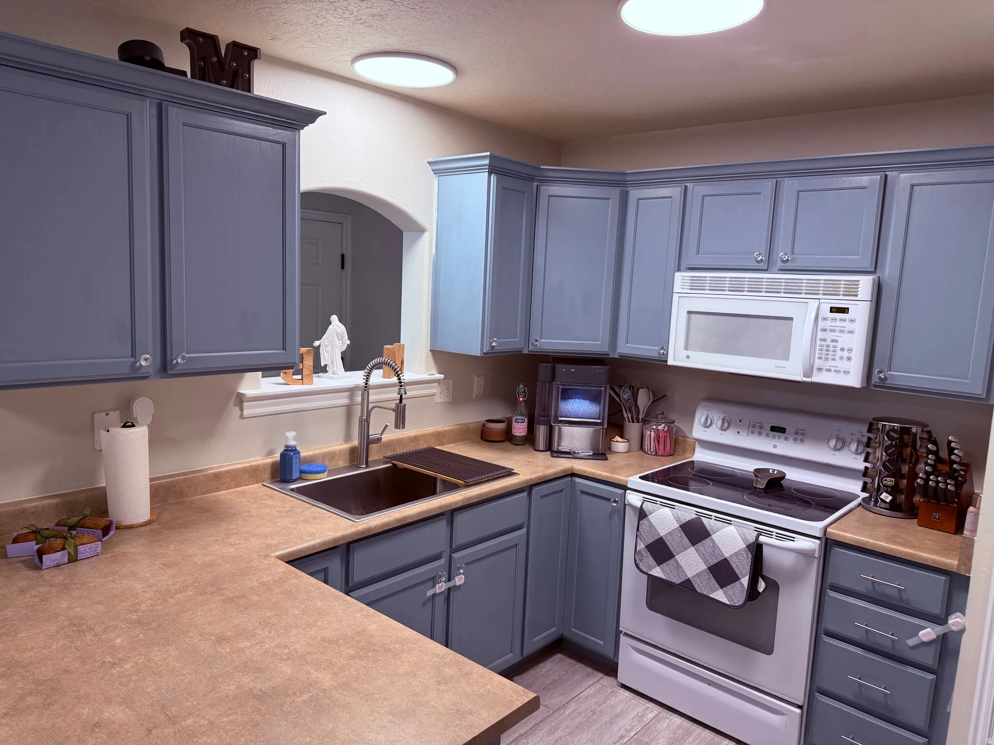 Kitchen featuring blue cabinetry, light-toned countertops, stainless steel sink, over-the-range microwave, and a white electric range