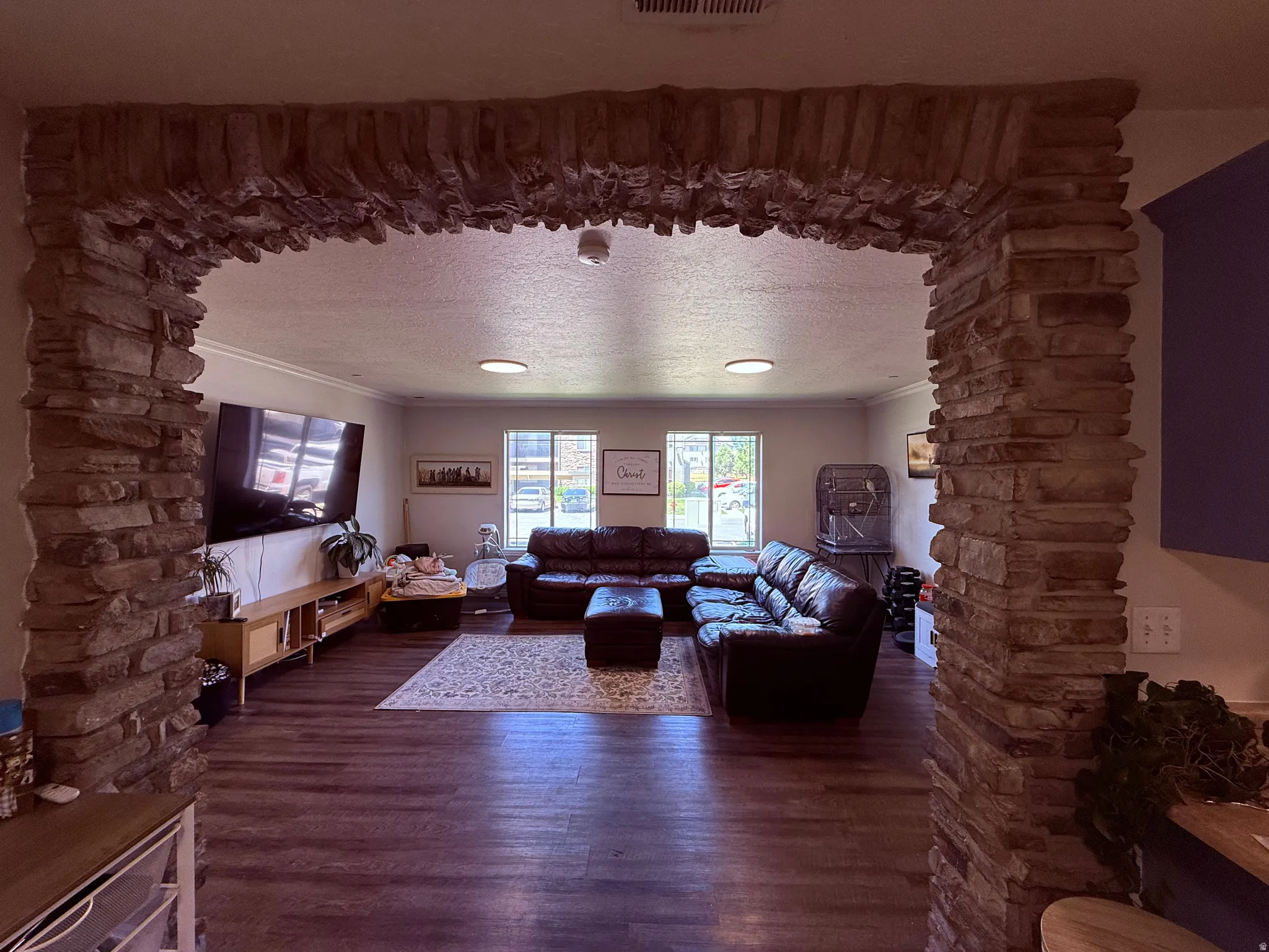 Stone archway opening to a living area featuring wood-finish flooring, white walls, and multiple windows