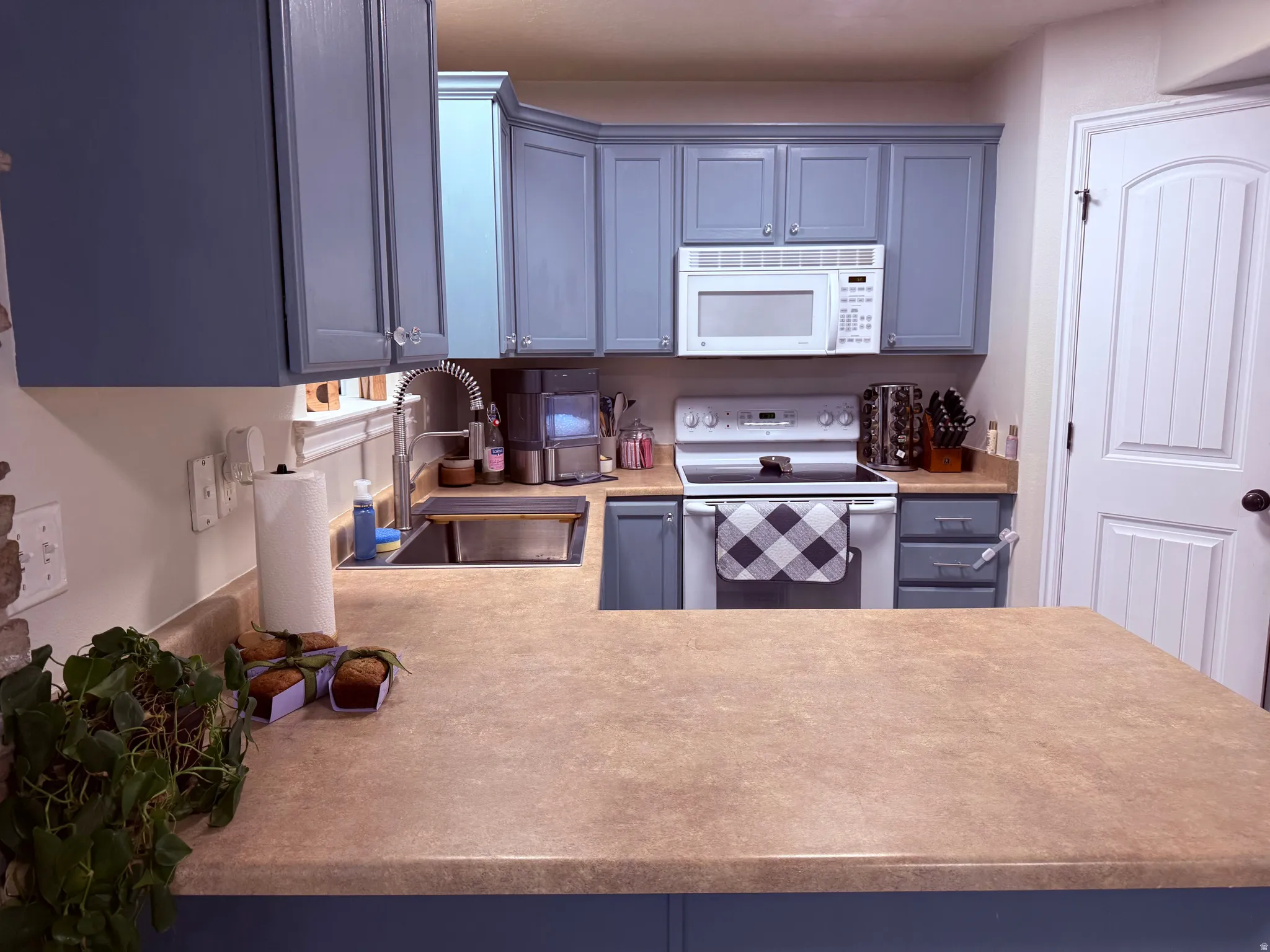 Kitchen featuring blue cabinetry, white appliances, a stainless steel sink with a gooseneck faucet, light-toned countertops, and a white paneled door