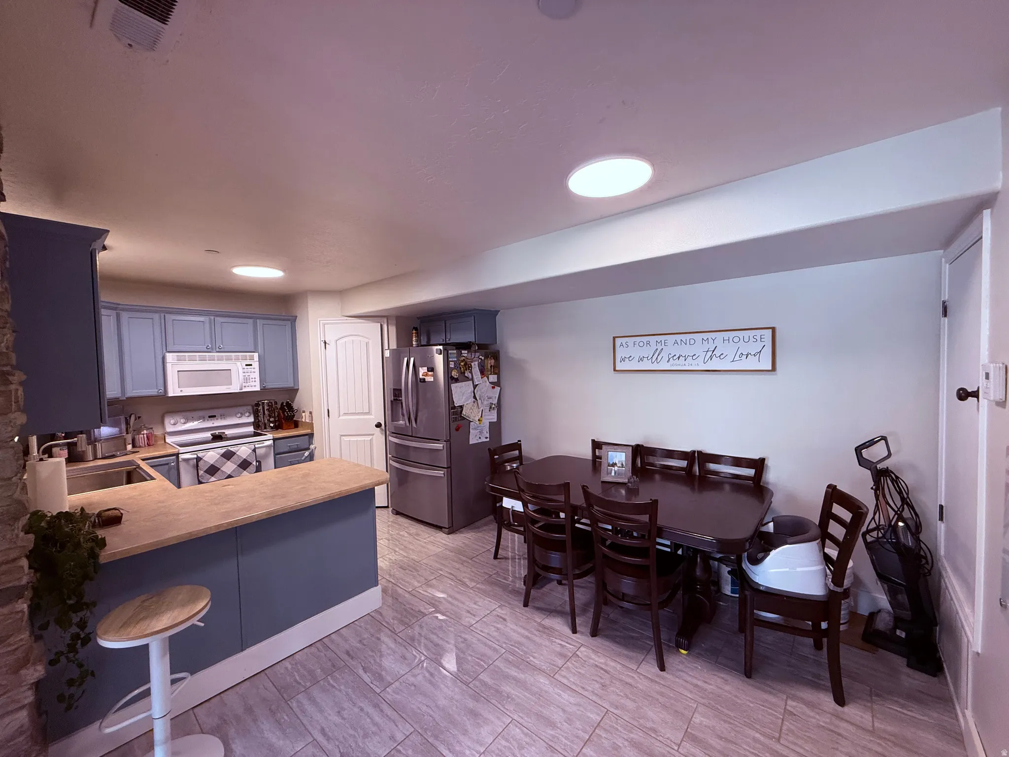 Open-concept kitchen and dining area featuring light blue cabinetry, stainless steel appliances, a wood-finish peninsula countertop, and tile flooring