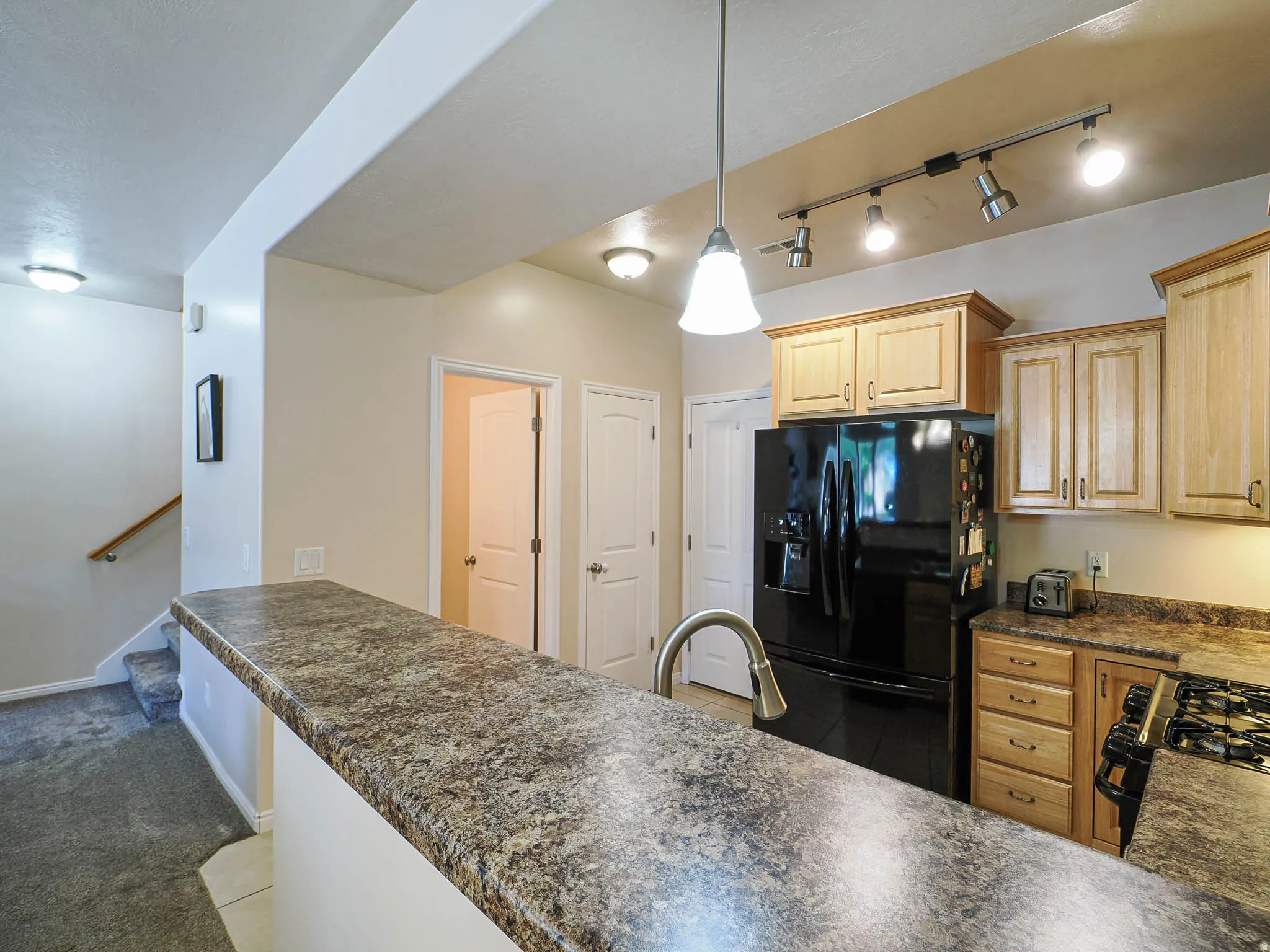 Kitchen featuring a peninsula with a patterned countertop, light wood cabinetry, and a black refrigerator