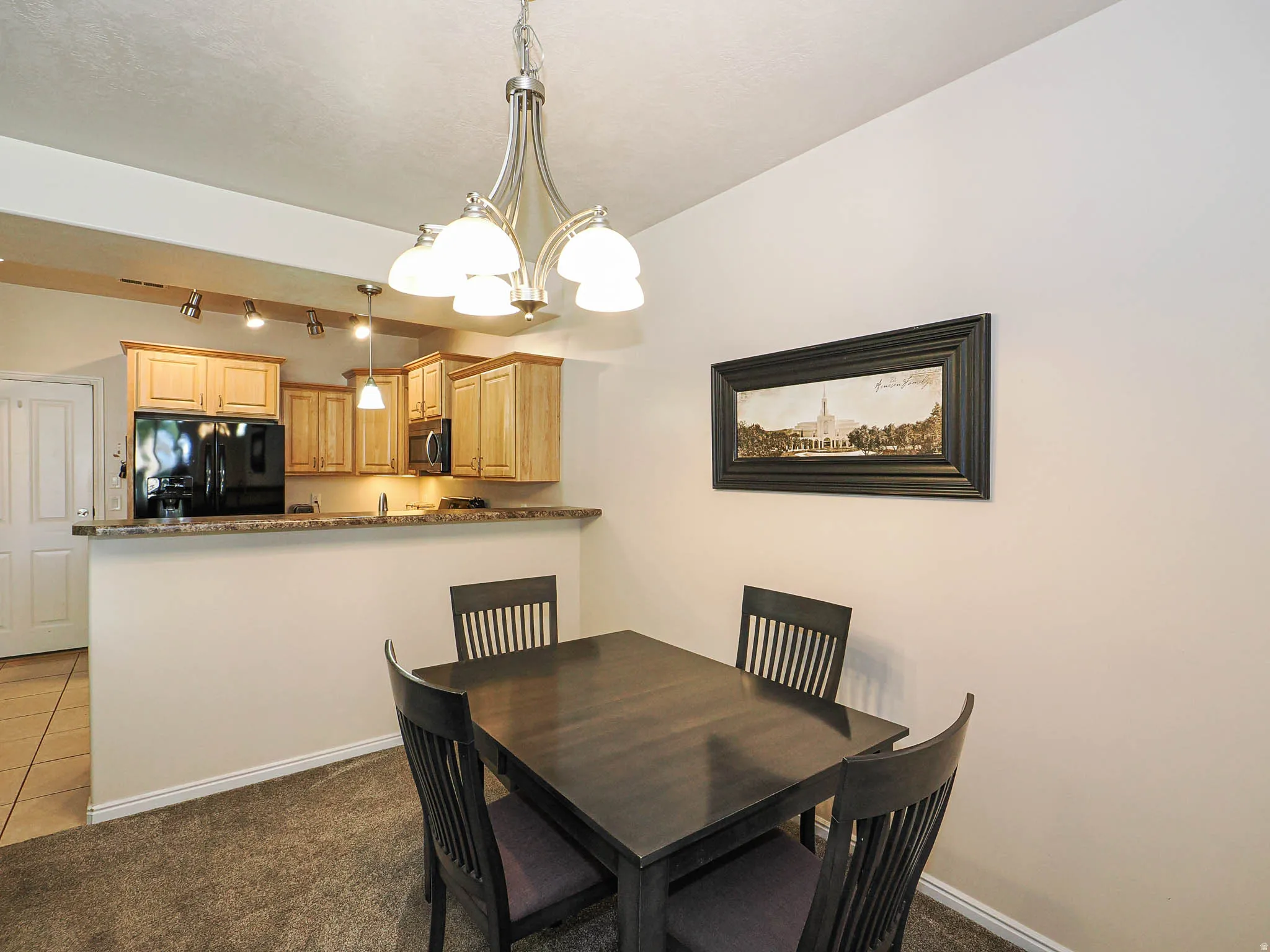 Open-concept dining space featuring a contemporary chandelier, carpeted flooring, and a breakfast bar with a stone-finish countertop