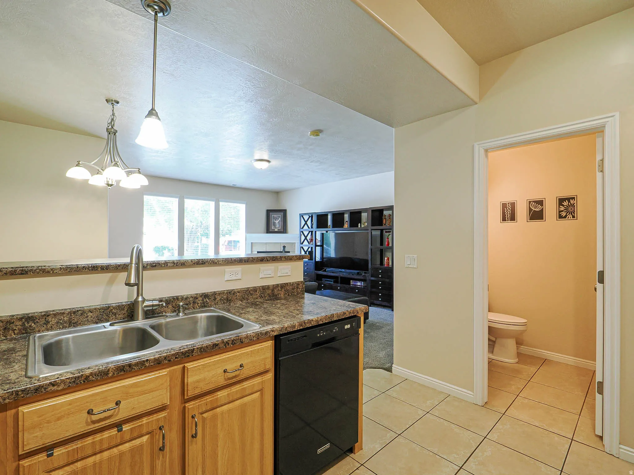 Kitchen area featuring a double basin stainless steel sink with a gooseneck faucet, light wood cabinetry, a black dishwasher, and granite-look countertops