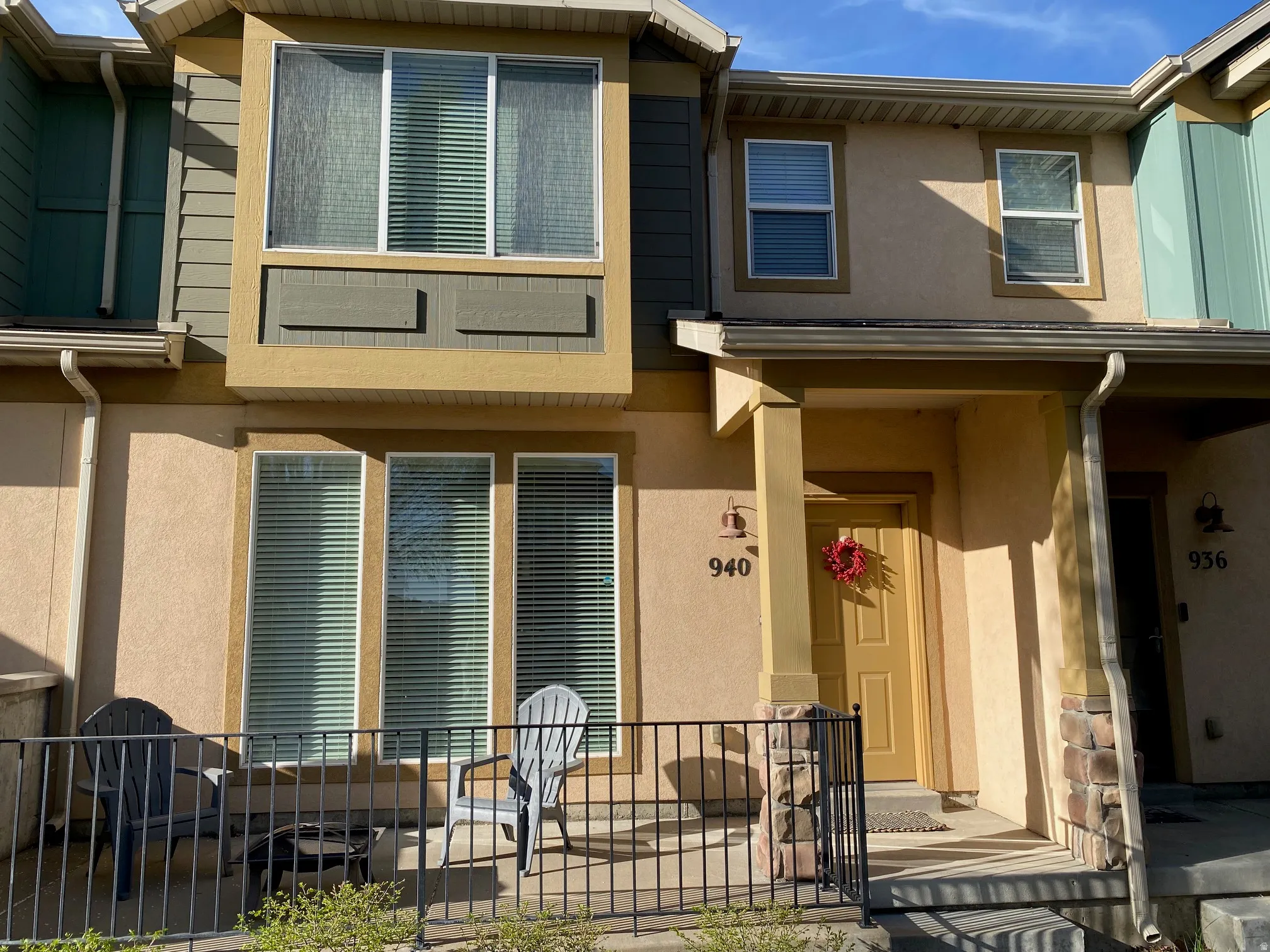 Front exterior featuring multi-textured facade, a covered entry with stone accents, a private patio with wrought iron fencing, and multiple windows with blinds