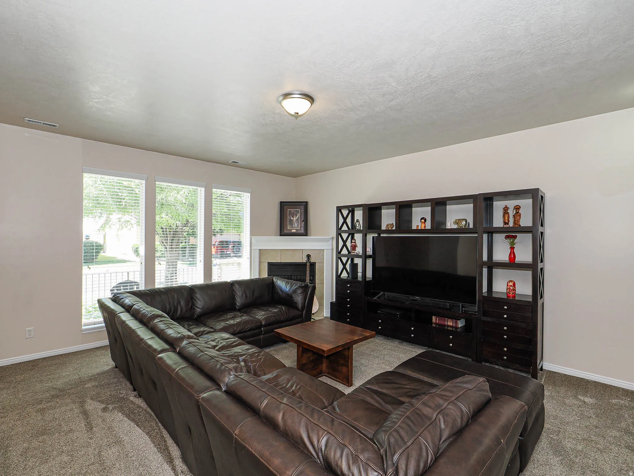 Carpeted living area featuring multiple windows with blinds, a built-in entertainment center, a fireplace with a mantel, and light-toned wall finishes