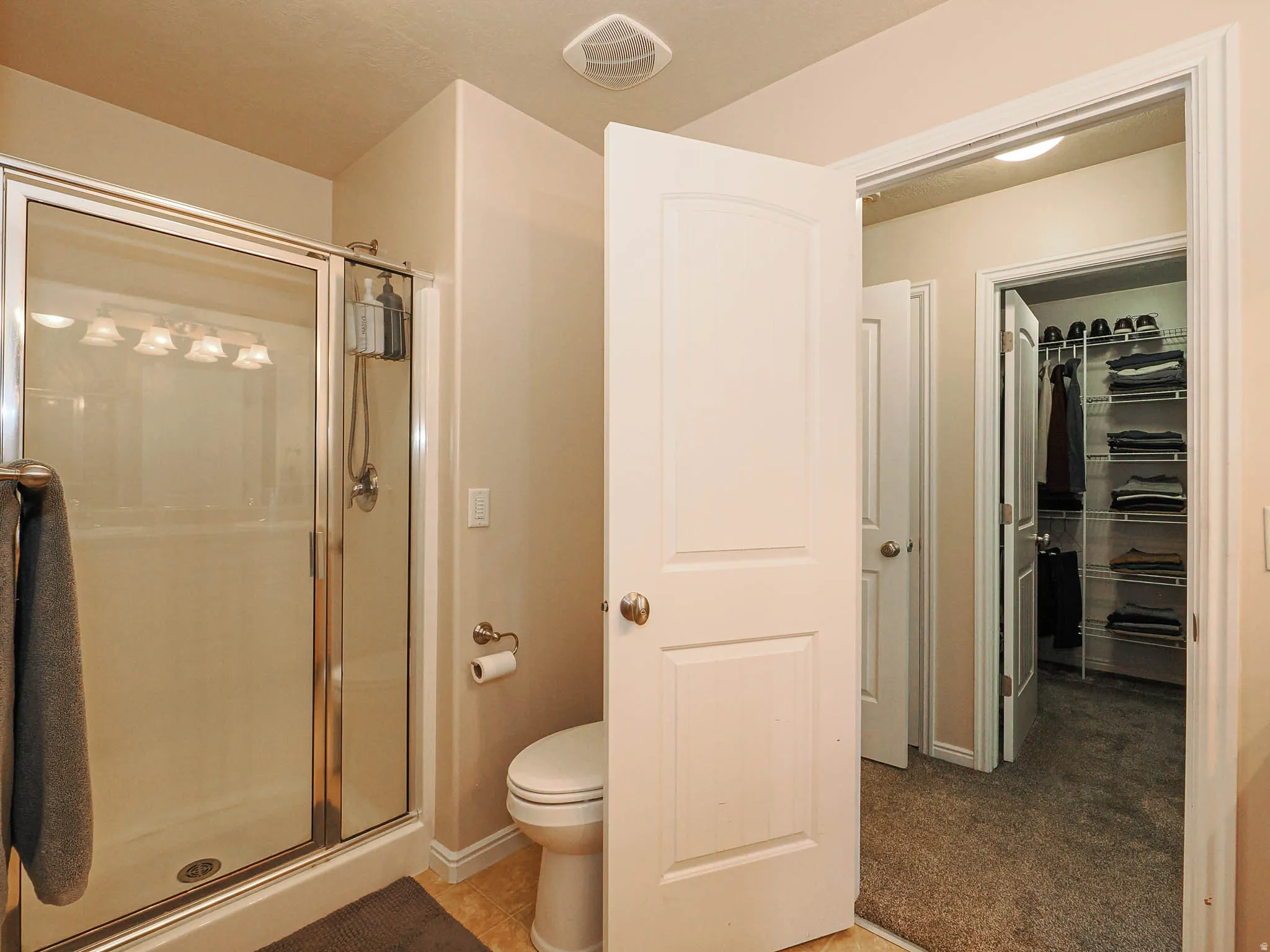 Shower enclosure with sliding glass doors, overhead light fixture, and a toilet