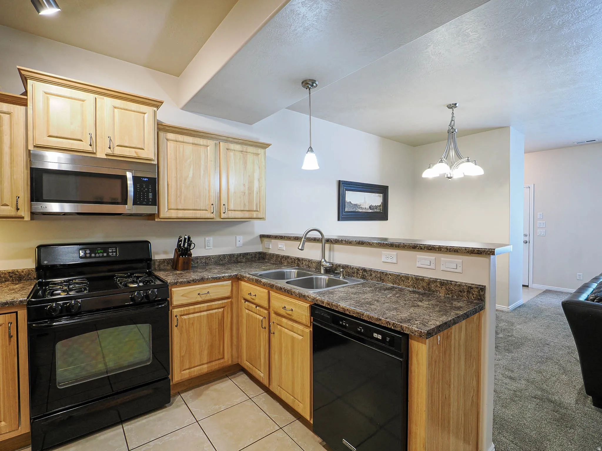 Kitchen featuring light wood cabinetry, stone-look countertops, and stainless steel appliances including a microwave and dishwasher