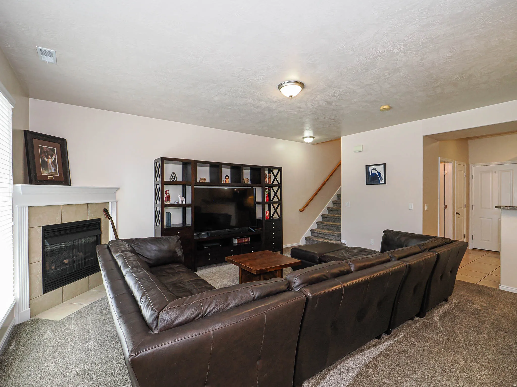 Living area featuring a tiled fireplace with a white mantel, light-toned walls, and grey carpet flooring