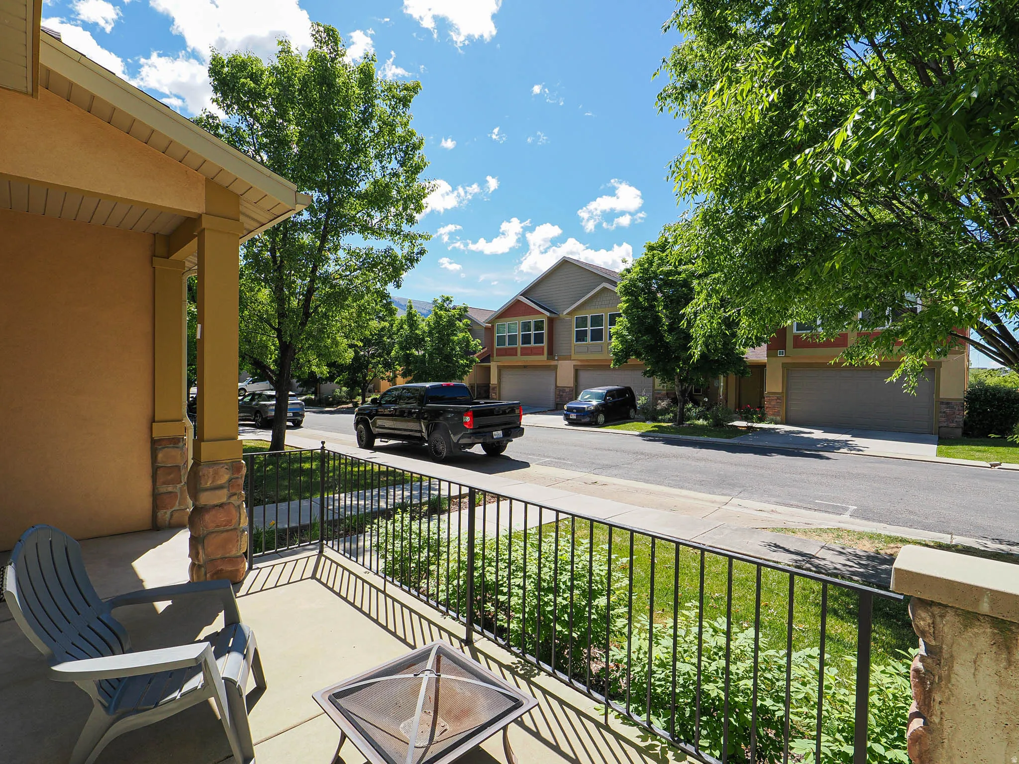 Covered front porch with stone-clad columns and a wrought iron railing, offering views of the street and mature trees