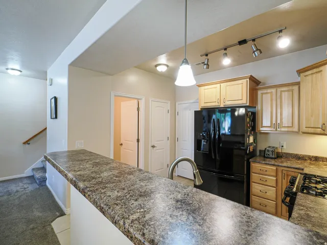 Kitchen featuring a peninsula with a patterned countertop, light wood cabinetry, and a black refrigerator