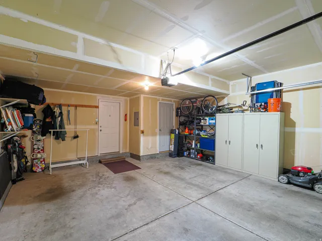 Spacious garage featuring a concrete floor, exposed ceiling joists, and multiple storage solutions